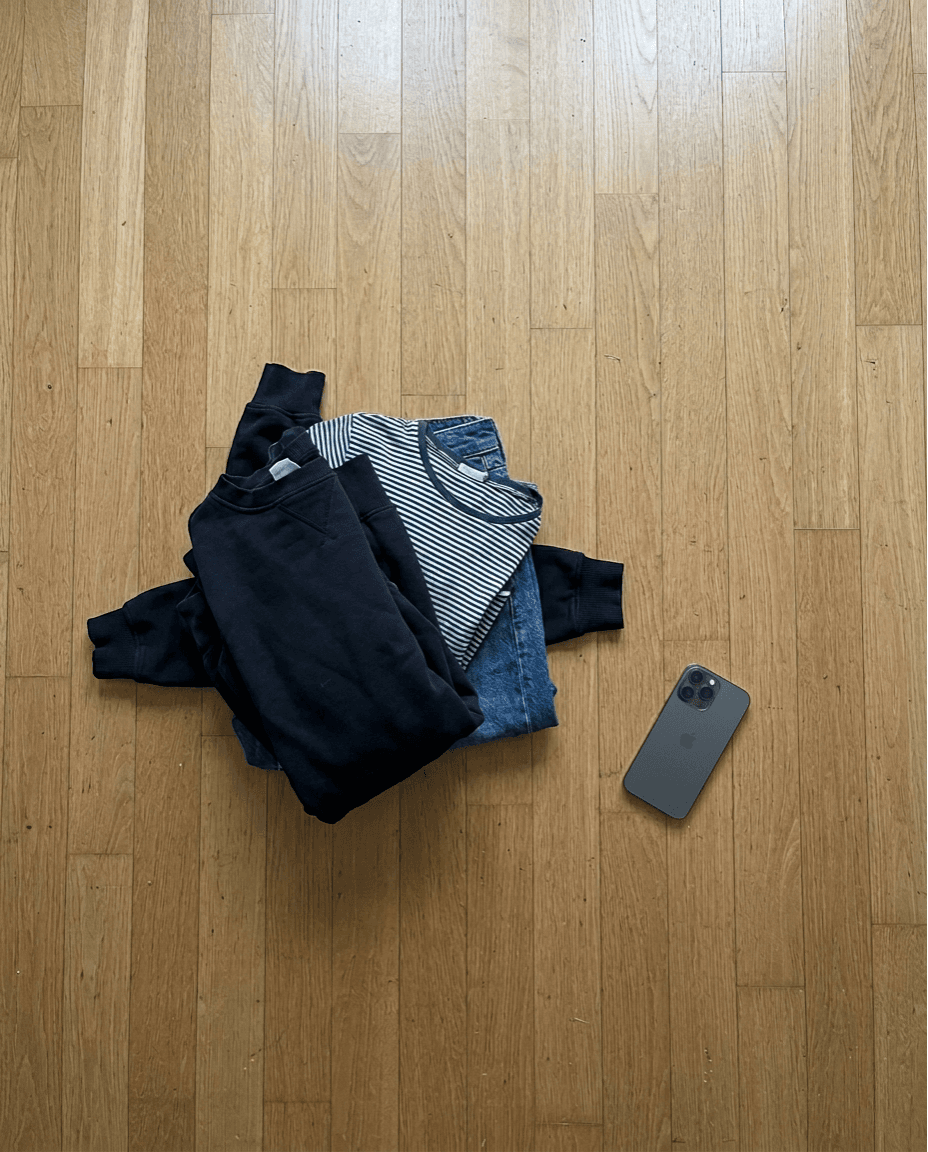 Petite pile de vêtements et iPhone face-down sur un parquet, ambiance fin de journée d'un reseller