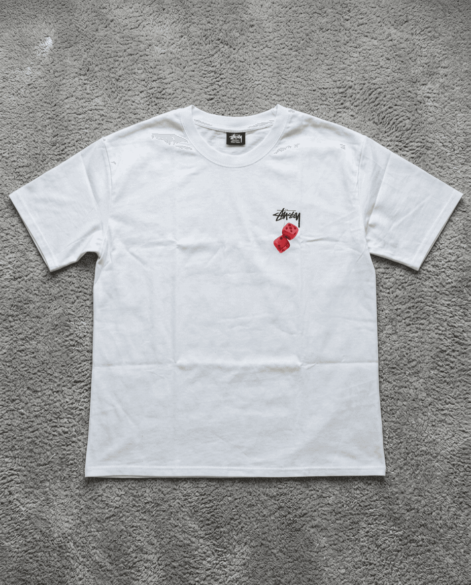 T-shirt Stussy blanc avec logo cursif rouge sur tapis gris